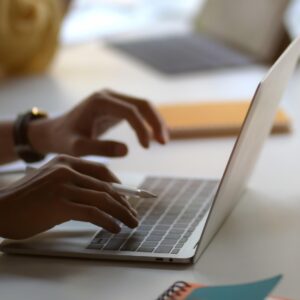 Περικομμένη φωτογραφία επιχειρηματία που πληκτρολογεί στο φορητό υπολογιστή με φλιτζάνι καφέ σε λευκό ξύλινο τραπέζι σε χώρο εργασίας